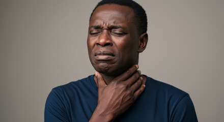Portrait of an African man experiencing discomfort while touching his neck, indicating sore throat or swollen lymph nodes. Neutral gray background. Concept of illness, discomfort, and medical attentio