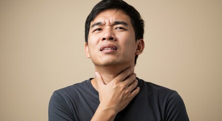 Portrait of an Asian man touching his neck with a pained expression, possibly suffering from sore throat, neck tension, or swollen lymph nodes. Neutral gray background. Healthcare and illness concept.