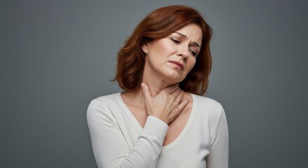 Portrait of a Caucasian woman touching her neck with a strained, painful expression, suggesting sore throat, inflamed glands, or general neck pain. Neutral gray background. Healthcare and medical conc