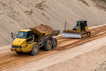 Heavy construction vehicles working on sandy site, dump truck and bulldozer leveling ground at...