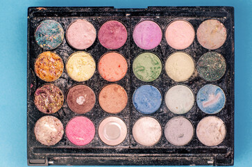 Colorful used eyeshadow palette with powder on blue background