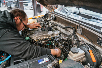 Mechanic working on engine s electrical system under open hood in auto repair workshop