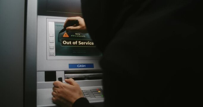 Unrecognizable Vandal in Hoodie Marking ATM Screen with Graffiti Using Marker Pen. Person Damaging Property, Vandalizing Out of Service Cash Machine with Illegal Graffiti. Vandalism in Public Place.