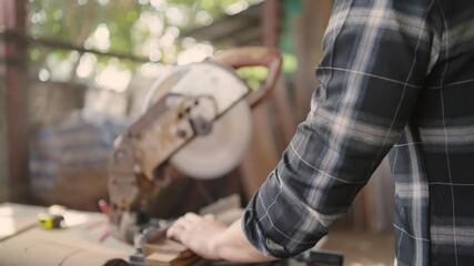 Male carpenter wearing protective eyewear using electric circular saw cutting wood board at workshop studio