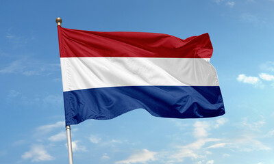 Waving national flag of the Netherlands with red, white and blue stripes in blue sky