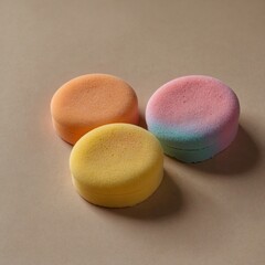 Two makeup sponges, one pink and one yellow, on a neutral beige surface.