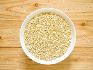 A bowl of uncooked white quinoa on wooden table