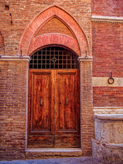 Elegant wooden door within a carved stone archway. The intricate details and textures highlight the region’s architectural charm. Travel to in Siena, Tuscany, Italy.