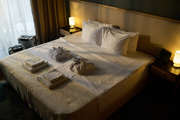 Luxurious setup with neatly arranged bed, towels, and bathrobes in well-lit hotel room. Suitcases, bedside lamps, and phone creating welcoming atmosphere