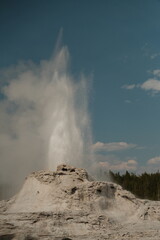 Castle Geyser erupting at yellowstone national park with fluffy clouds in sky