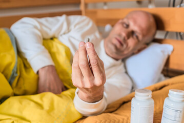 Man suffering from insomnia headache taking pill while lying in bed. Man lying in bed holding a capsule in hand, medicine bottles nearby, concept of supplements or morning routine.