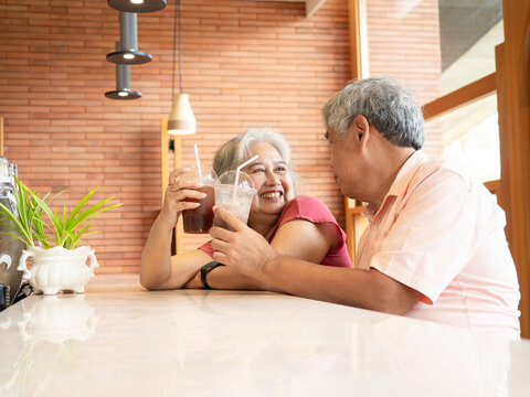 Senior Asian couple sitting at a cafe, smiling at the camera, enjoying coffee and reading together.