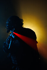 Soldier in tactical gear aiming weapon with illuminated scope against dramatic lighting