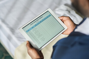 Person holding tablet with business report spreadsheet visible on screen, reviewing data. Close-up...