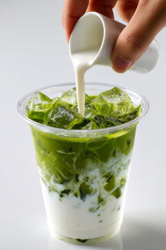 Iced matcha latte with milk being poured, refreshing green tea drink with ice cubes in clear plastic cup