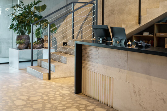 Modern office interior featuring minimalistic design with a staircase and potted plants enhancing the ambiance. Front desk with devices adds to the sleek and organized look