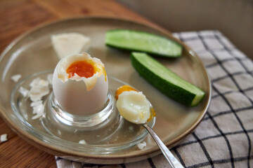 Morning breakfast, top view of a ceramic plate with a boiled egg, cucumber, and a piece of cheese