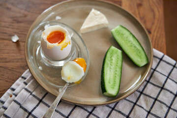 Morning breakfast, top view of a ceramic plate with a boiled egg, cucumber, and a piece of cheese