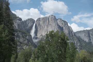Scenery with granite cliffs, greenery, cascading waterfalls , puffy clouds and blue skies at...