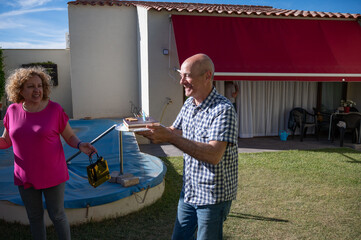 Smiling senior man holding tray with cakes while woman gestures casually in backyard