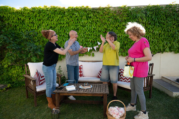 Group of happy seniors clapping and smiling during festive outdoor birthday celebration in a cozy backyard with decorations and cake