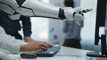 A close-up of a robotic arm assisting a person at a keyboard in a modern office, emphasizing collaboration between humans and machines for data tasks.Noogenesis