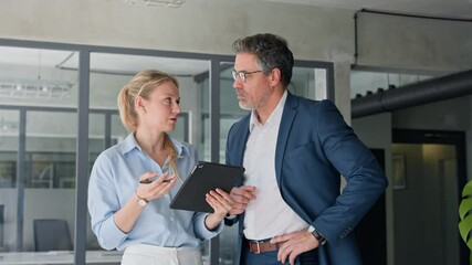 Two partners, team of professional business people working, discussing work project. Mature focused senior mentor leader man showing young woman manager project on tablet touchscreen pc pad in office - Powered by Adobe