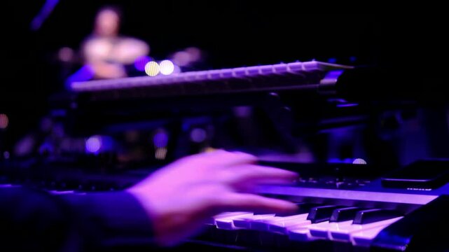 a musician's hand playing a keyboard synthesizer on stage lighting during a live performance, rehearsal of a rock concert, capturing the electronic music vibe and the atmosphere of the event
