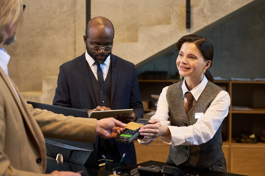 Concierge processing a payment at hotel front desk with two clients present. Person in background holding tablet and dressed in business attire