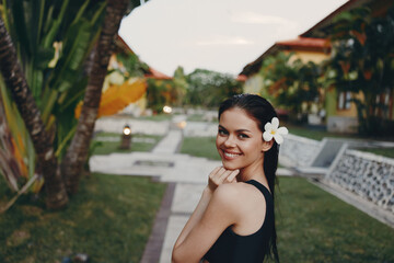 Woman with a Flower in Her Hair Standing in Front of Palm Trees and Grass on a Sunny Day