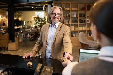 Elderly man with friendly smile greeting receptionist in modern, open office space with shelves and diverse seating in background