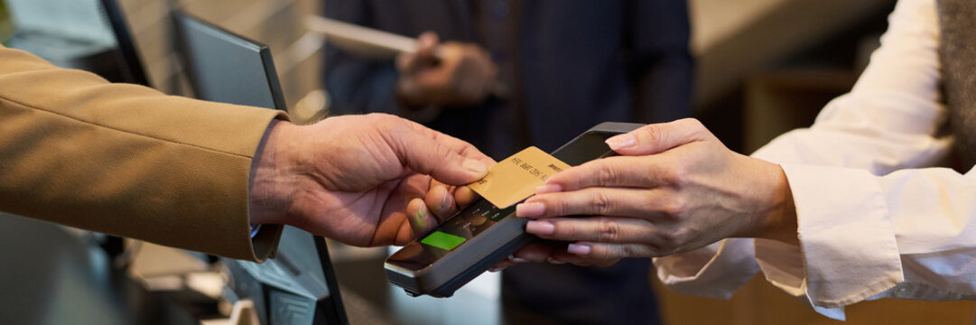 Close-up of hands exchanging credit card at checkout terminal during payment process. Handing over card for transaction at modern point-of-sale device