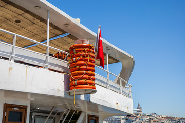 Stacked lifebuoys and waving Turkish flag on ferry deck with Galata Tower in the background, Istanbul
