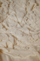 Close-up of soft white fabric with deep folds lying on a bed in warm natural light. Ideal for...