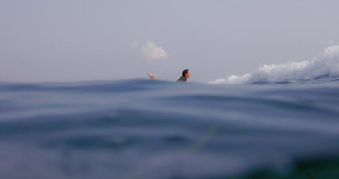 Woman rowing on surfboard in ocean with crashing waves. Surf girl on longboard during surfing.