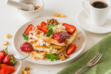 Belgian waffles with cottage cheese cream, strawberries, walnuts and mint on a white plate on a light table with a cup of coffee. Delicious, Sunday breakfast.