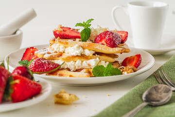 Belgian waffles with cottage cheese cream, strawberries, walnuts and mint on a white plate on a light table with a cup of coffee. Delicious, Sunday breakfast.