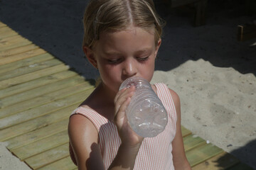Little girl having water break on the beach to avoid dehydration and heat illness. Concept of...
