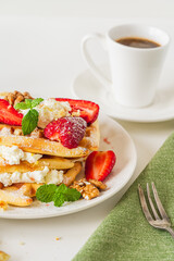 Belgian waffles with cottage cheese cream, strawberries, walnuts and mint on a white plate on a light table with a cup of coffee. Delicious, Sunday breakfast.