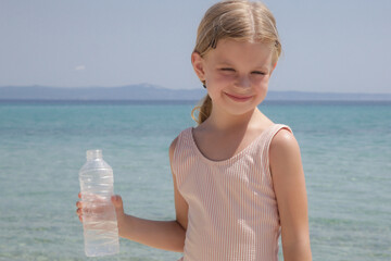 Little girl having water break on the beach to avoid dehydration and heat illness. Concept of...