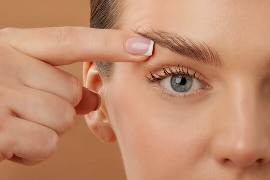 Blepharoplasty. Woman touching eyelid skin and pointing to the wrinkles on the upper eyelid, closeup shot over beige background