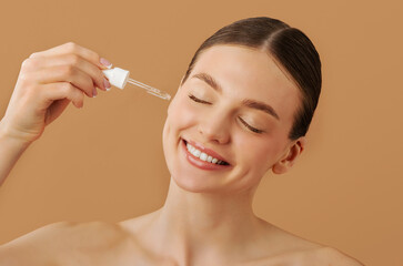 Facial cosmetics concept. Happy young European woman holding pipette with beauty product, applying...