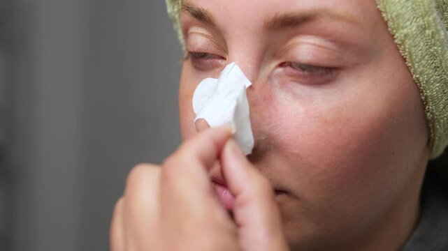 Woman gently peels off nose strip for blackhead removal during personal skincare care.