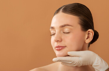Young lady with smooth skin receiving inspecting of face, cosmetologist in rubber gloves touching...