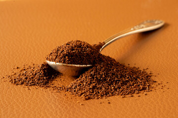 Spoon with ground coffee beans on brown leather background, morning drink