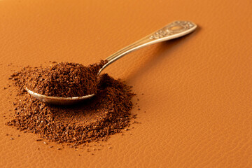 Spoon with ground coffee beans on brown leather background, morning drink