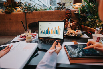 Colleagues collaborate and brainstorm with visual charts using laptops during a dynamic business meeting, emphasizing teamwork and analytic problem-solving in a contemporary workspace.