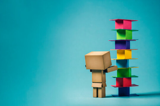 A cardboard man builds a tower out of colored boxes. Space for text.