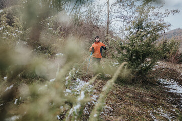 A person dressed in an orange jacket walks through a forested area covered in snow, showcasing an...