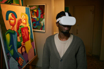 Individual wearing virtual reality headset while standing in art gallery with abstract paintings on...